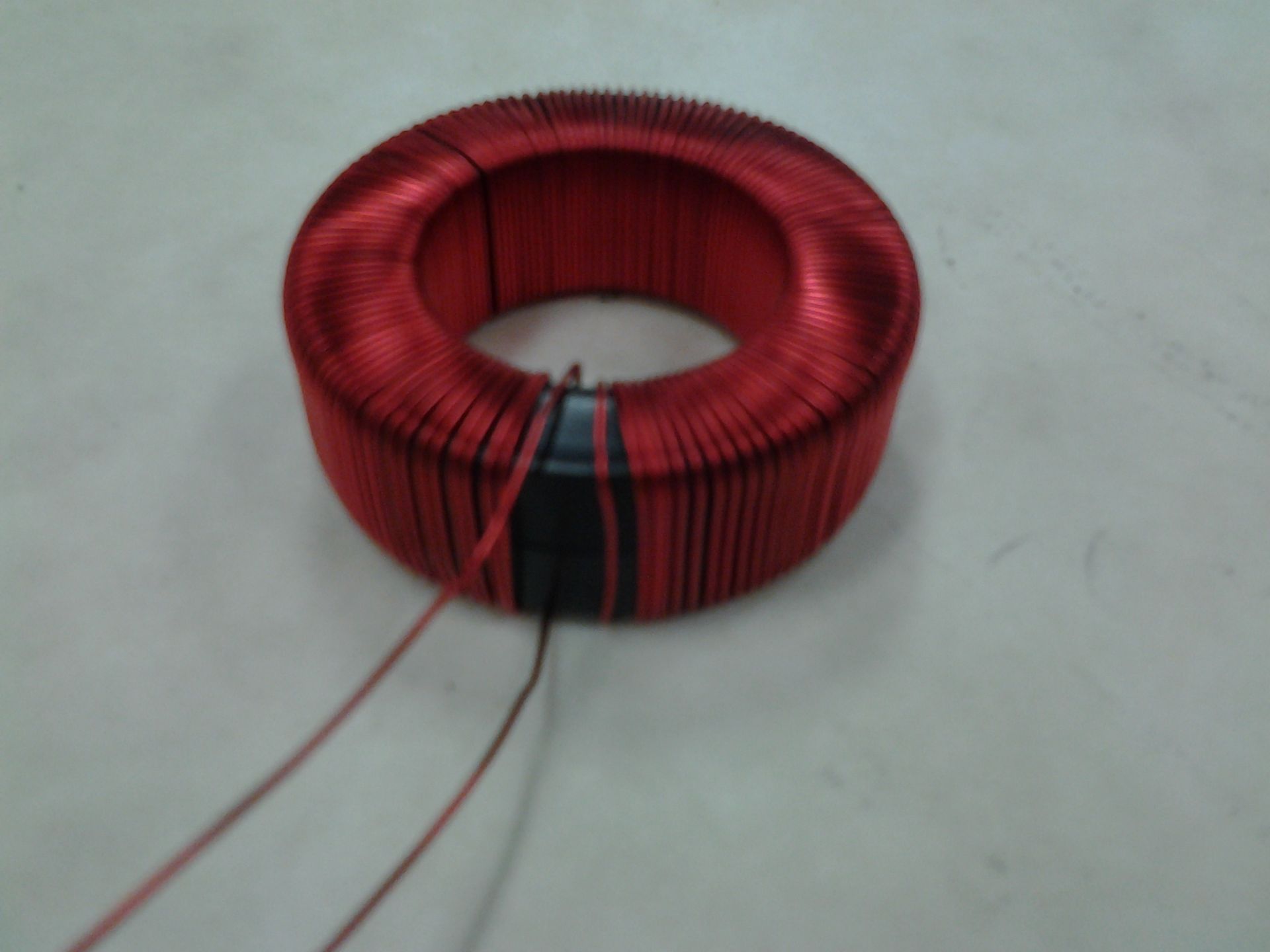 Red toroidal transformer with wires on a white surface