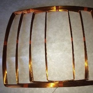 Copper wire coil in a rectangular shape with vertical parallel wires, on a light-colored surface