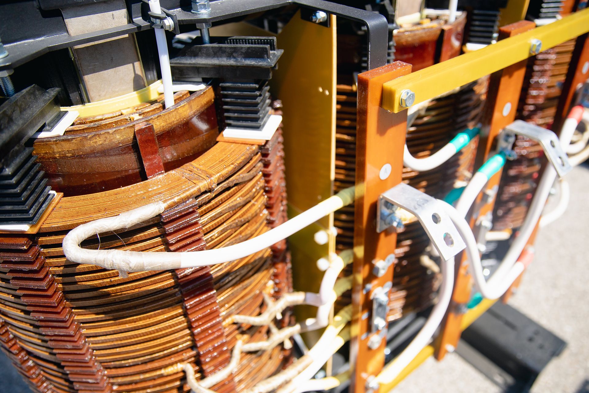 Close-up of a large electrical transformer with copper coils, white wiring, and yellow/brown insulation