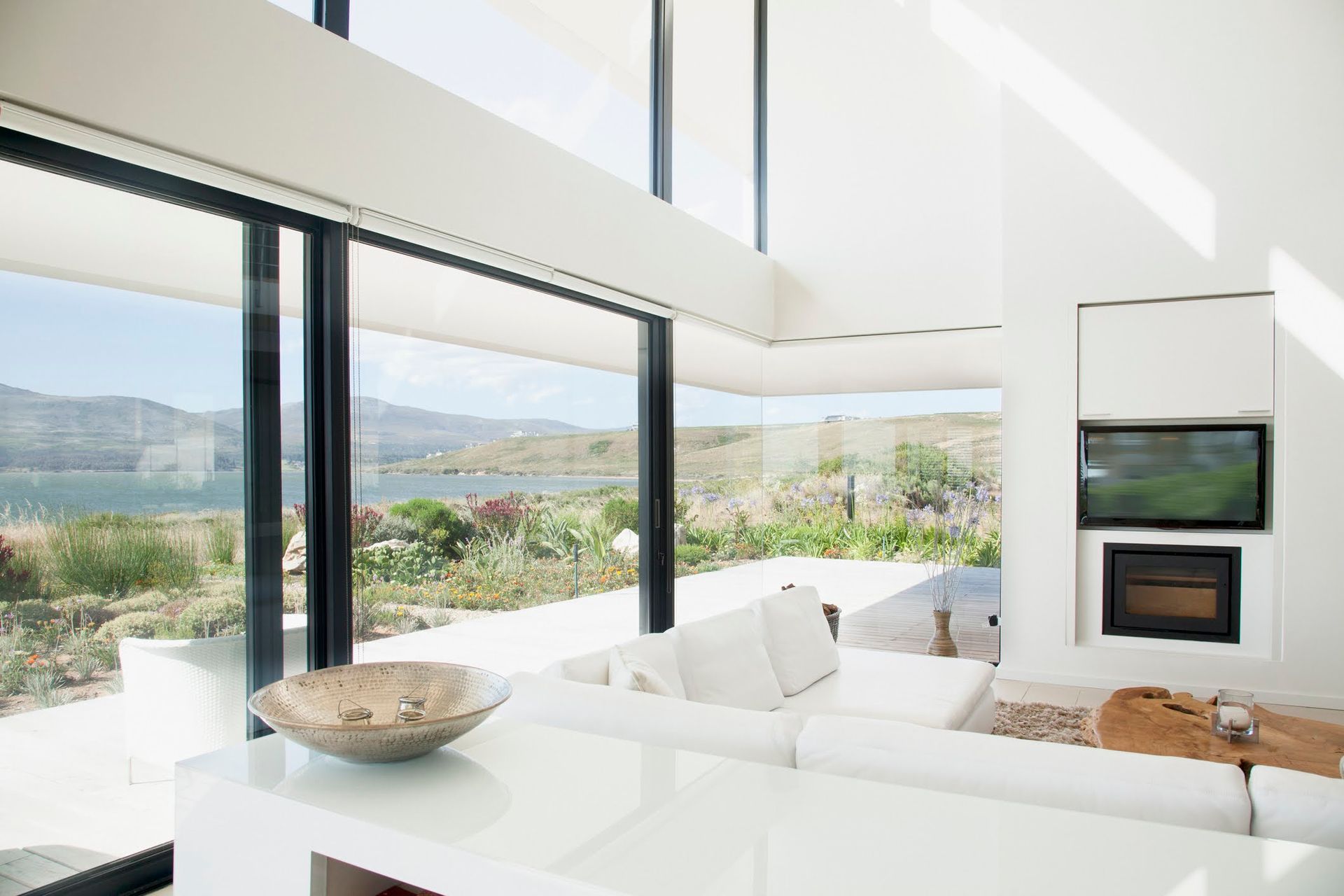 Soggiorno moderno con ampie finestre, pareti bianche e vista sull'acqua e sul verde.