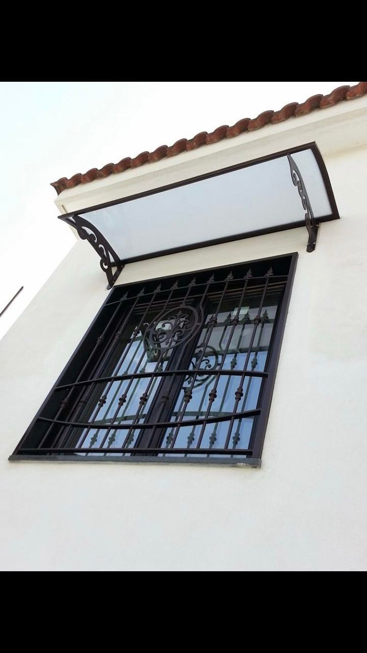 Finestra in metallo nero con inferriate decorate, sotto una tenda bianca su un edificio color crema.