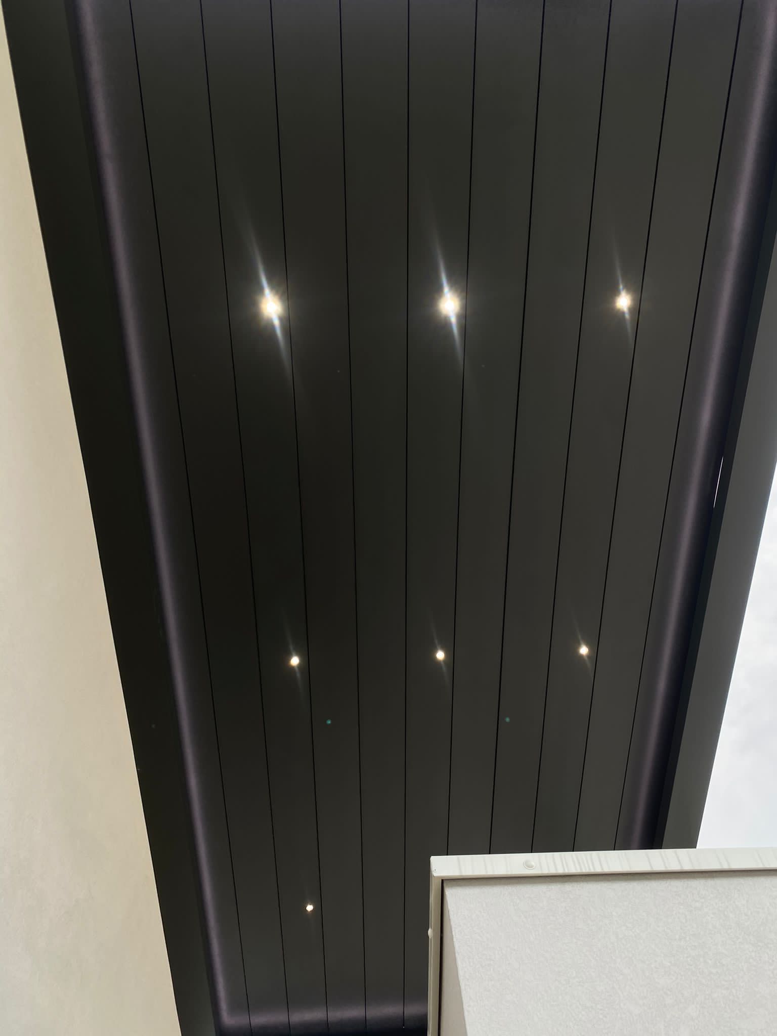 Soffitto grigio scuro con luci da incasso e perforazioni lineari.
