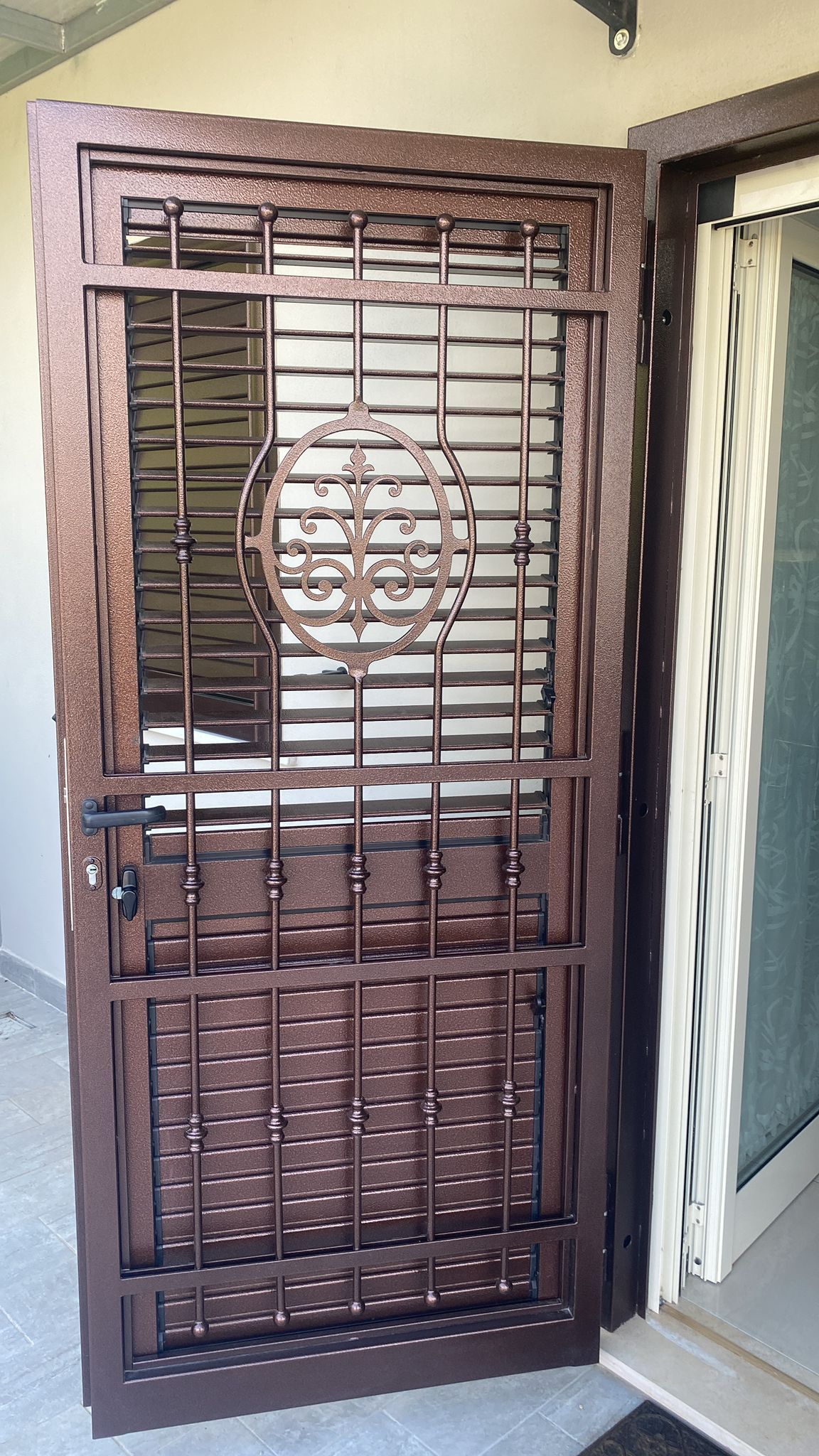 Porta di sicurezza in metallo marrone con barre orizzontali e verticali e design centrale decorativo.