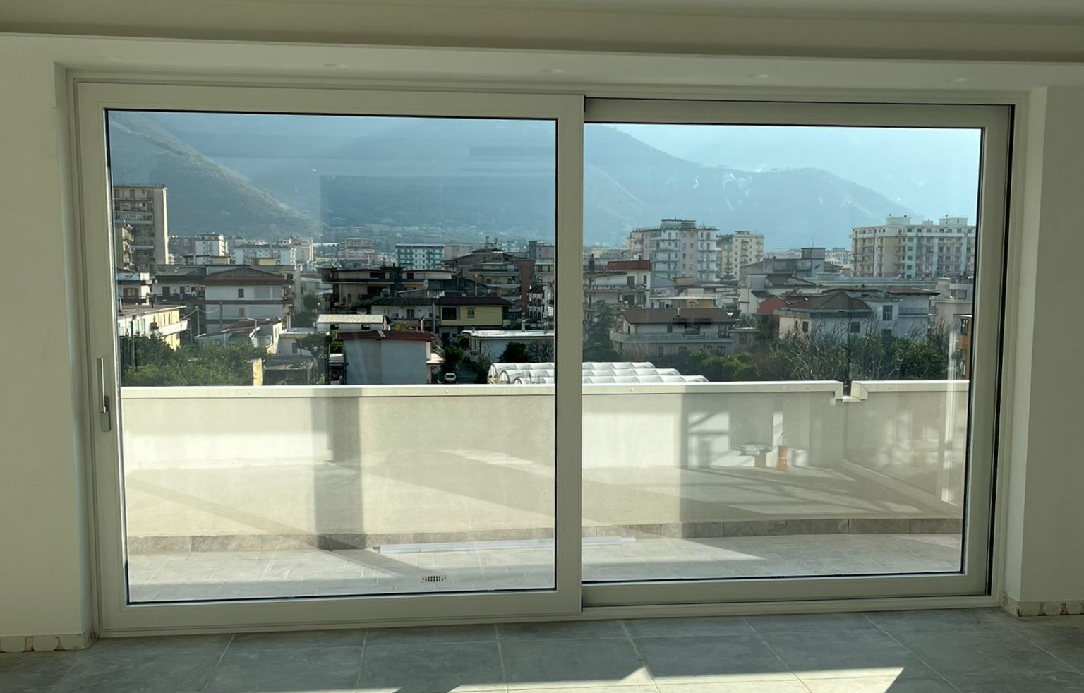 Porta scorrevole in vetro con vista sulla città da uno spazio interno, con finiture bianche e tetto.