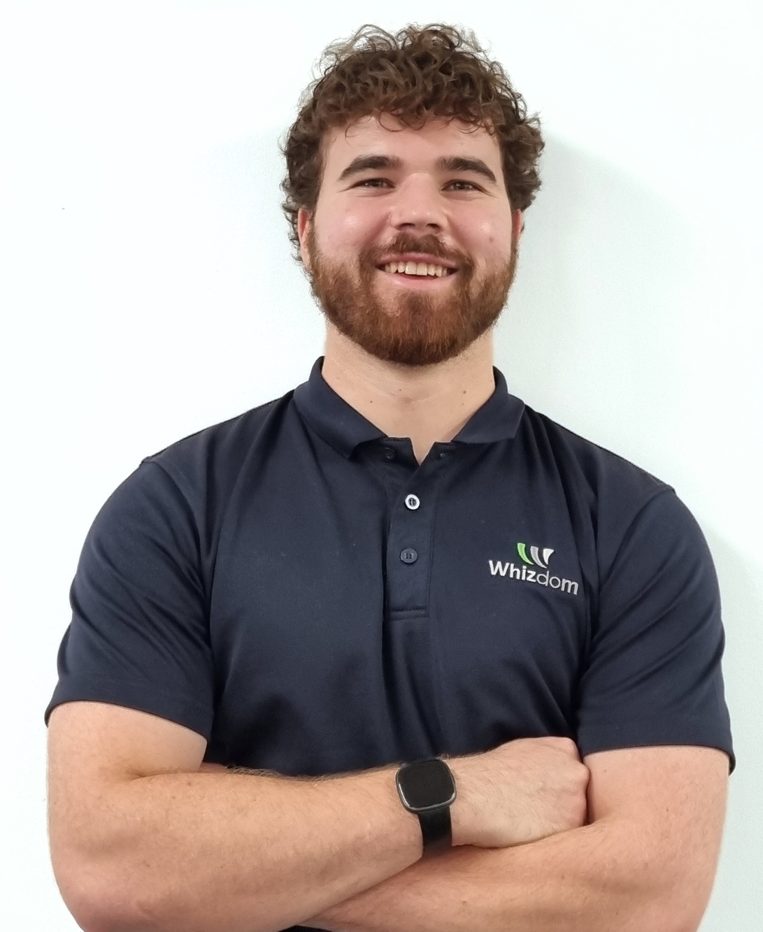 Man with brown curly hair and beard, smiling, arms crossed, wearing a dark blue polo shirt.
