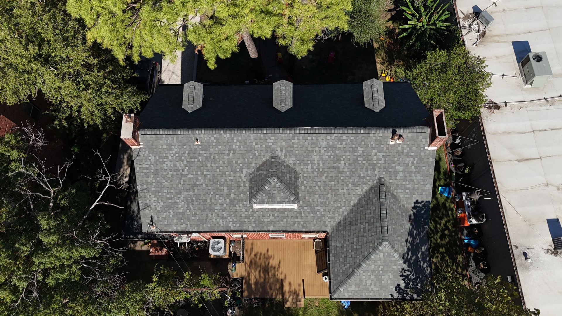Overhead view of a gray-roofed house with three chimneys and surrounding trees.