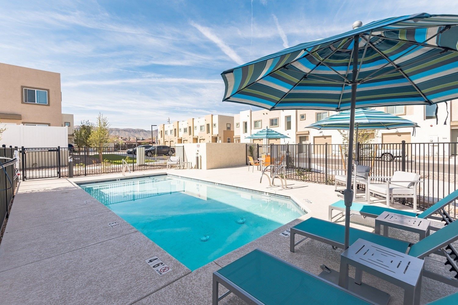 Apartment pool deck with turquoise umbrellas and lounge chairs beside a clear swimming pool