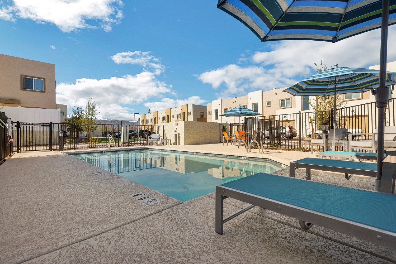 Apartment courtyard with a swimming pool, lounge chairs, and striped umbrellas under a blue sky