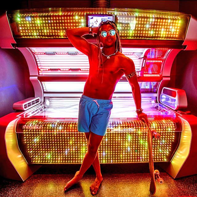 Stylischer Mann mit Skateboard vor beleuchtetem P9 Solarium bei SunWorld – Sonnenstudio mit Wow-Effekt.