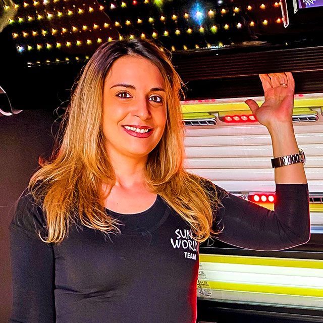 Freundliche SunWorld Mitarbeiterin steht vor moderner Sonnenbank – persönliche Beratung inklusive.