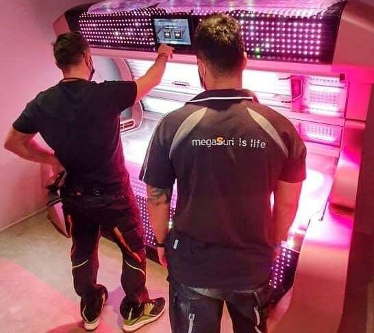 Zwei Solariumtechniker führen eine Funktionskontrolle an einem Solarium im SunWorld Studio durch.