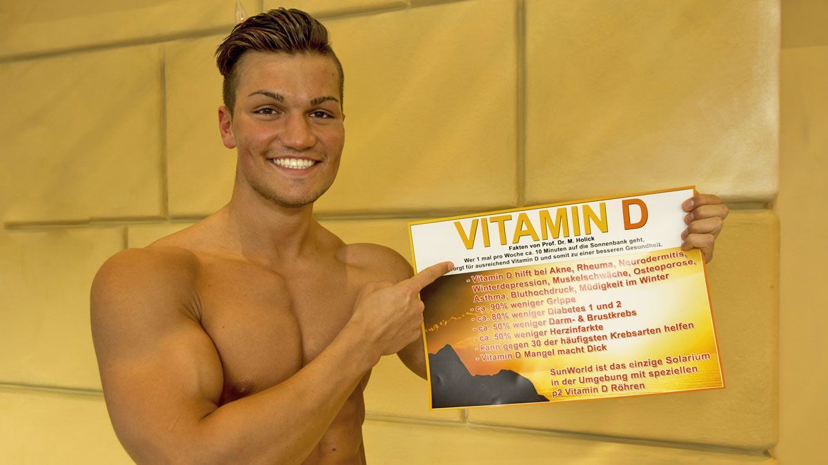 Sportlicher Mann präsentiert ein Plakat mit gesundheitlichen Vorteilen von Vitamin D – aufgenommen im SunWorld Solarium.