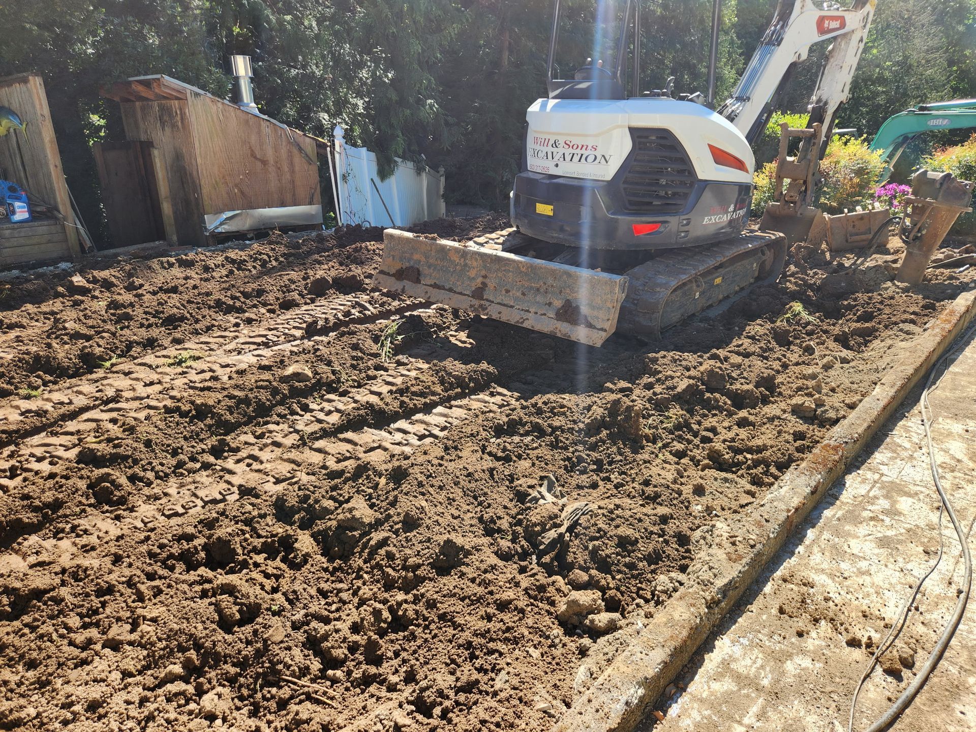 A small excavator on muddy ground, preparing a trench along a concrete edge.