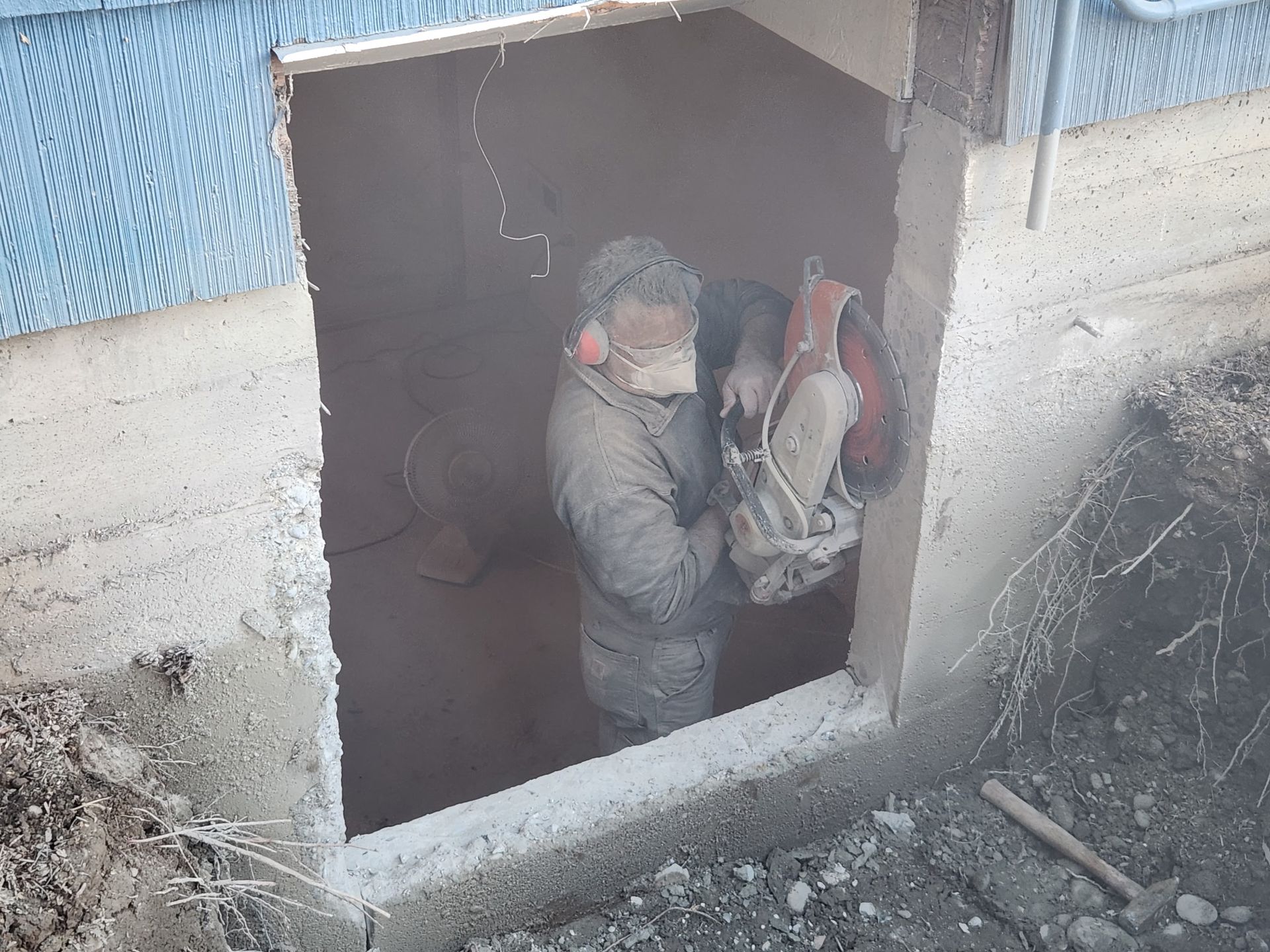 Person cutting concrete with a saw, creating a rectangular opening in a wall. Dusty work site.
