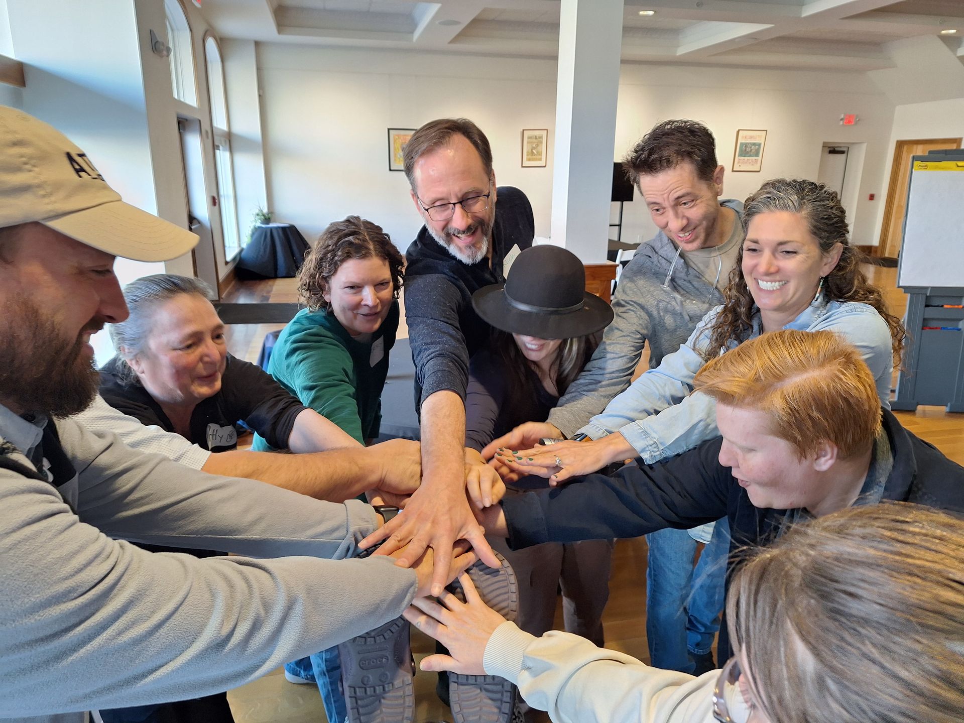 Group of smiling people in a circle placing their hands together in the middle of the group