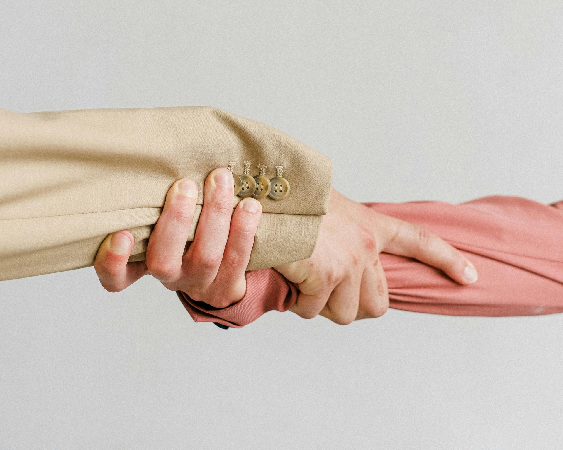 Two people holding hands; one in a tan sleeve, the other in a pink sleeve, against a white background.