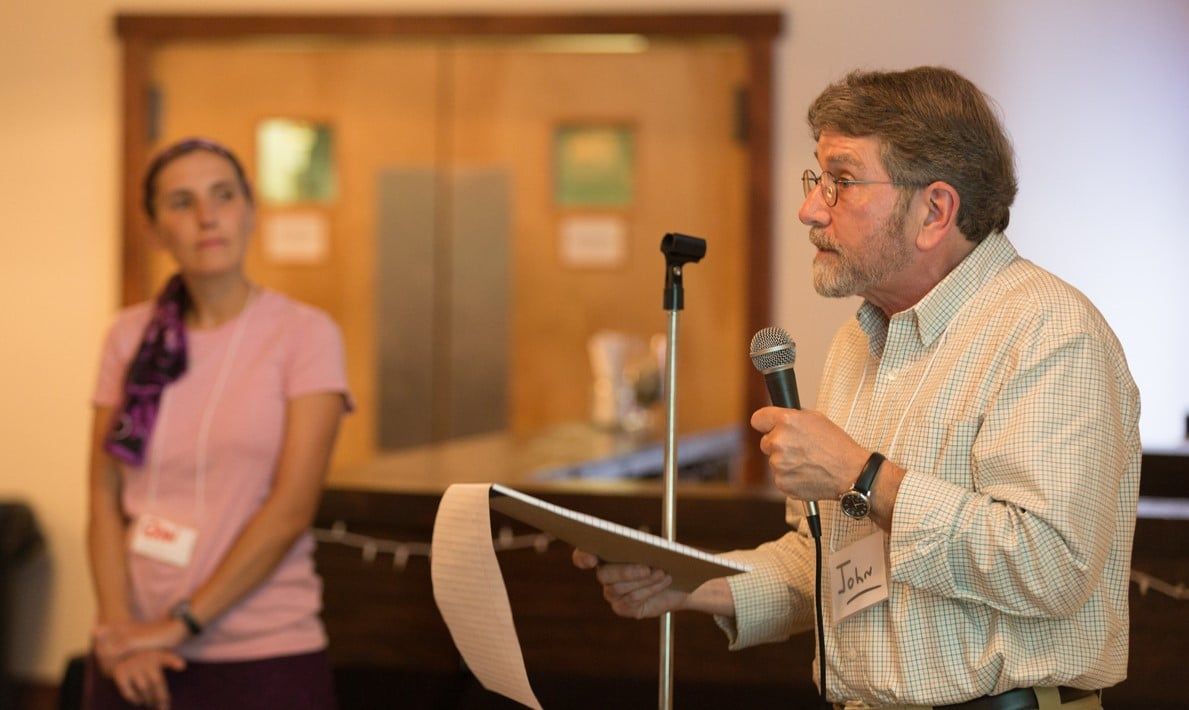 A man is speaking into a microphone while a woman stands behind him