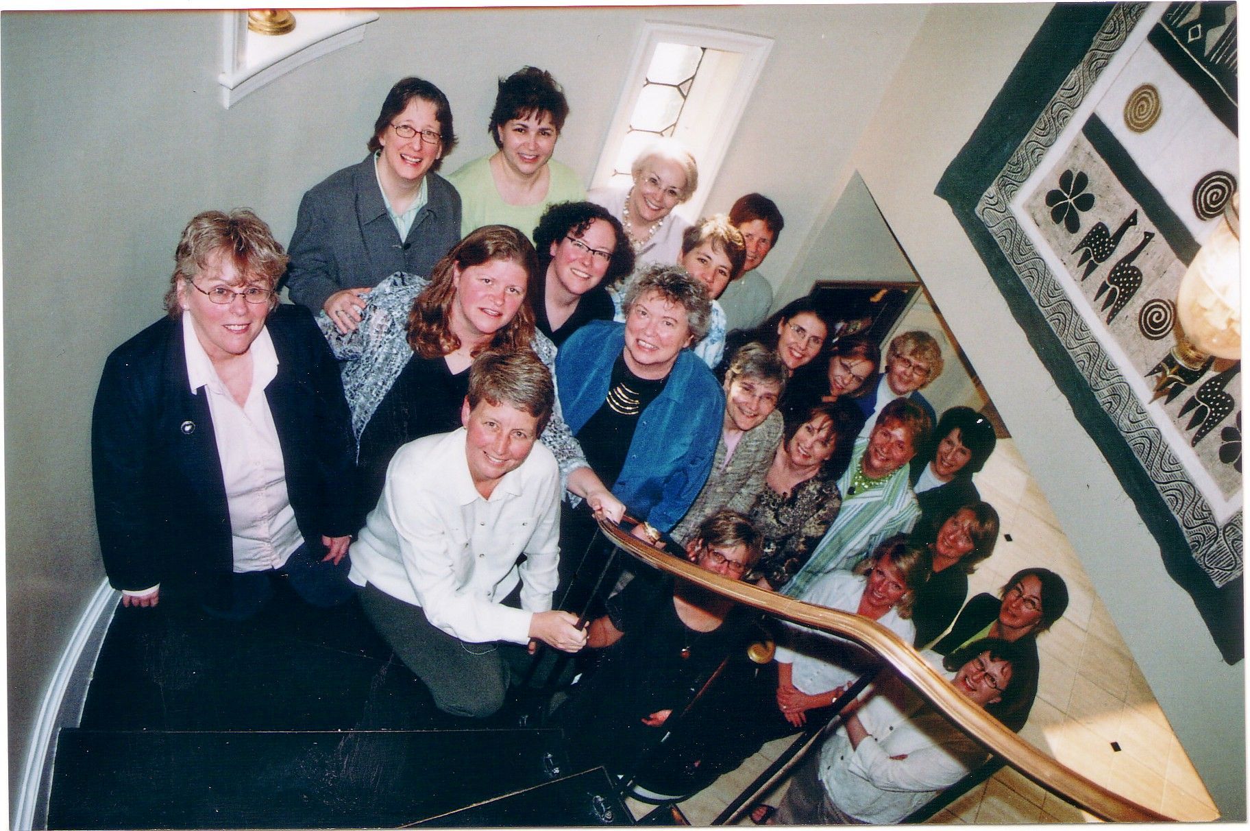 Group of women on a staircase, smiling and looking at the camera. Warm colors, many expressions.
