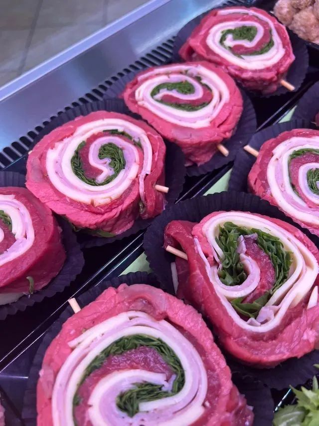 Tramezzini rosa arrotolati con ripieno bianco e verde su un vassoio