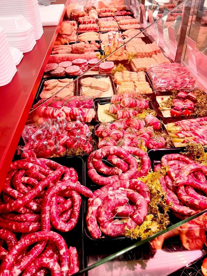 Banco frigo con vassoi di salsicce crude assortite e tagli di carne rossa illuminati da luci rosa.