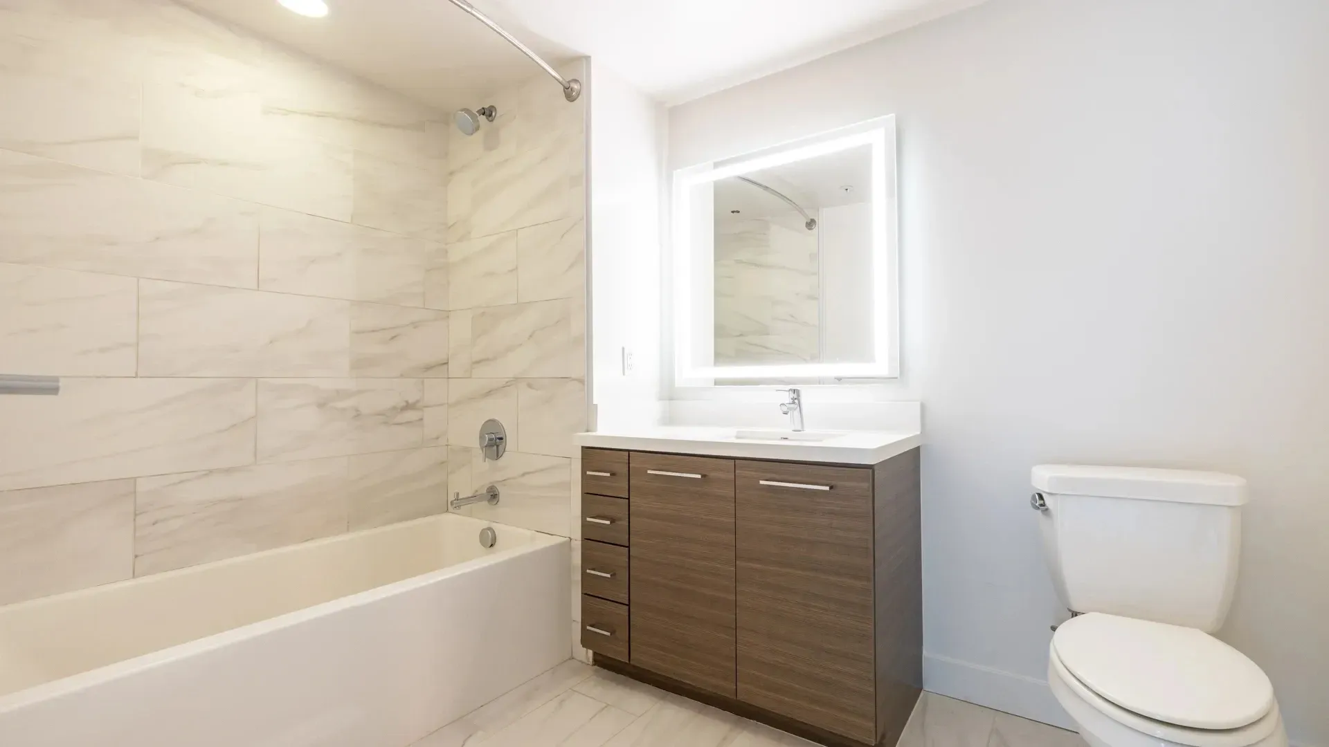 Bathroom with a modern vanity, illuminated mirror, and a bathtub.