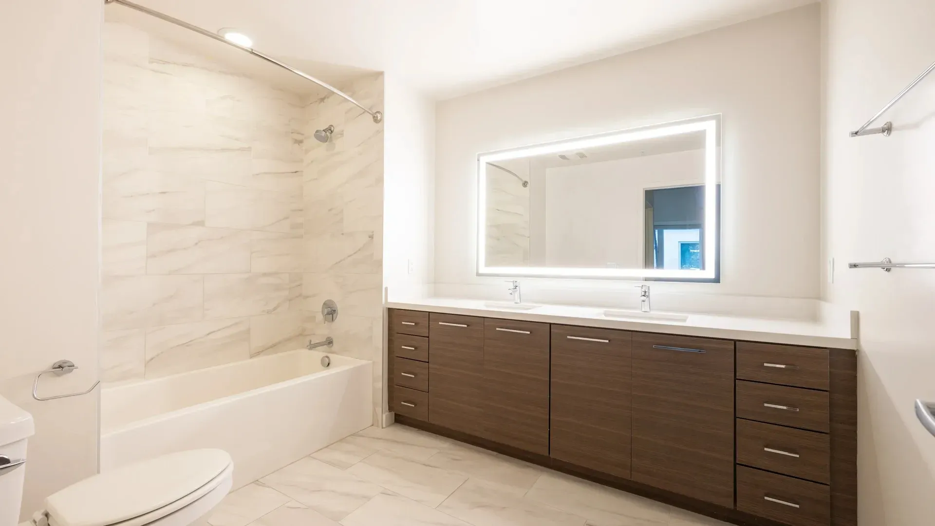 Modern bathroom with double vanity, large illuminated mirror, and bathtub.