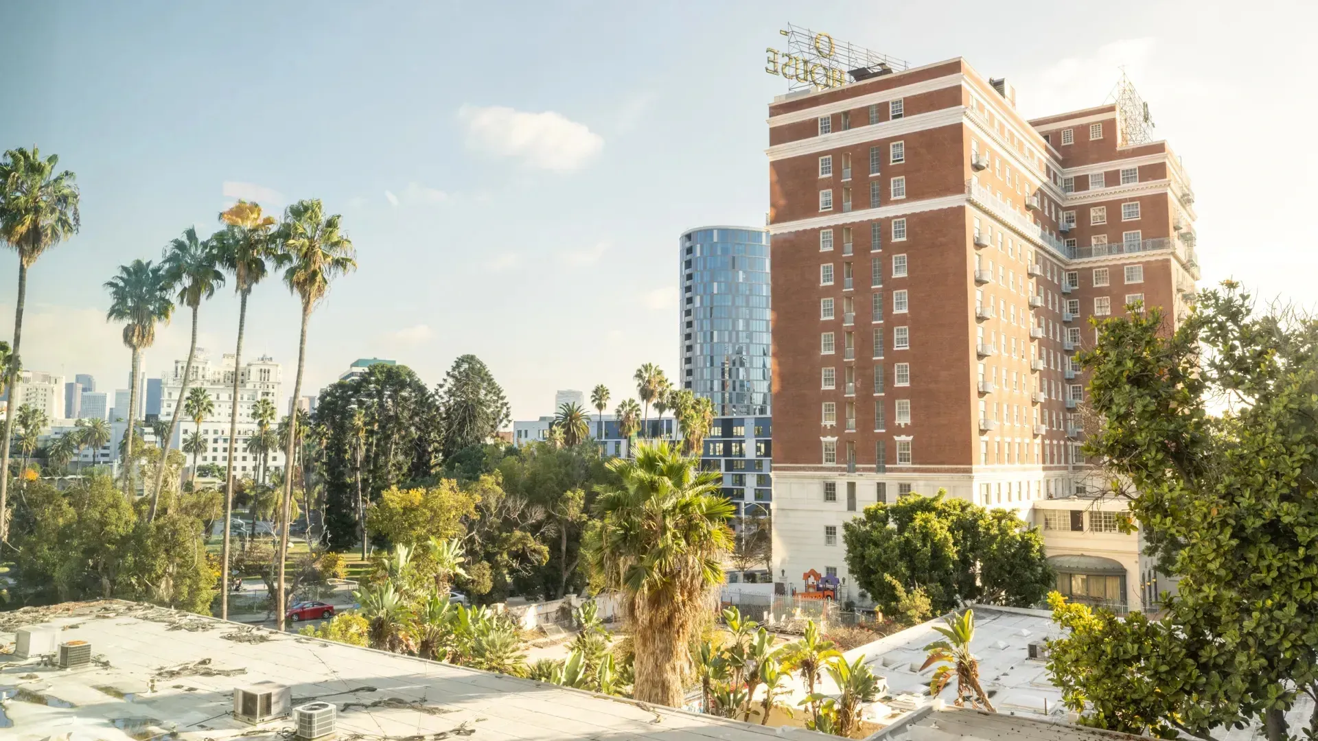 View of a historic brick building with a rooftop sign and palm trees, overlooking a city skyline.