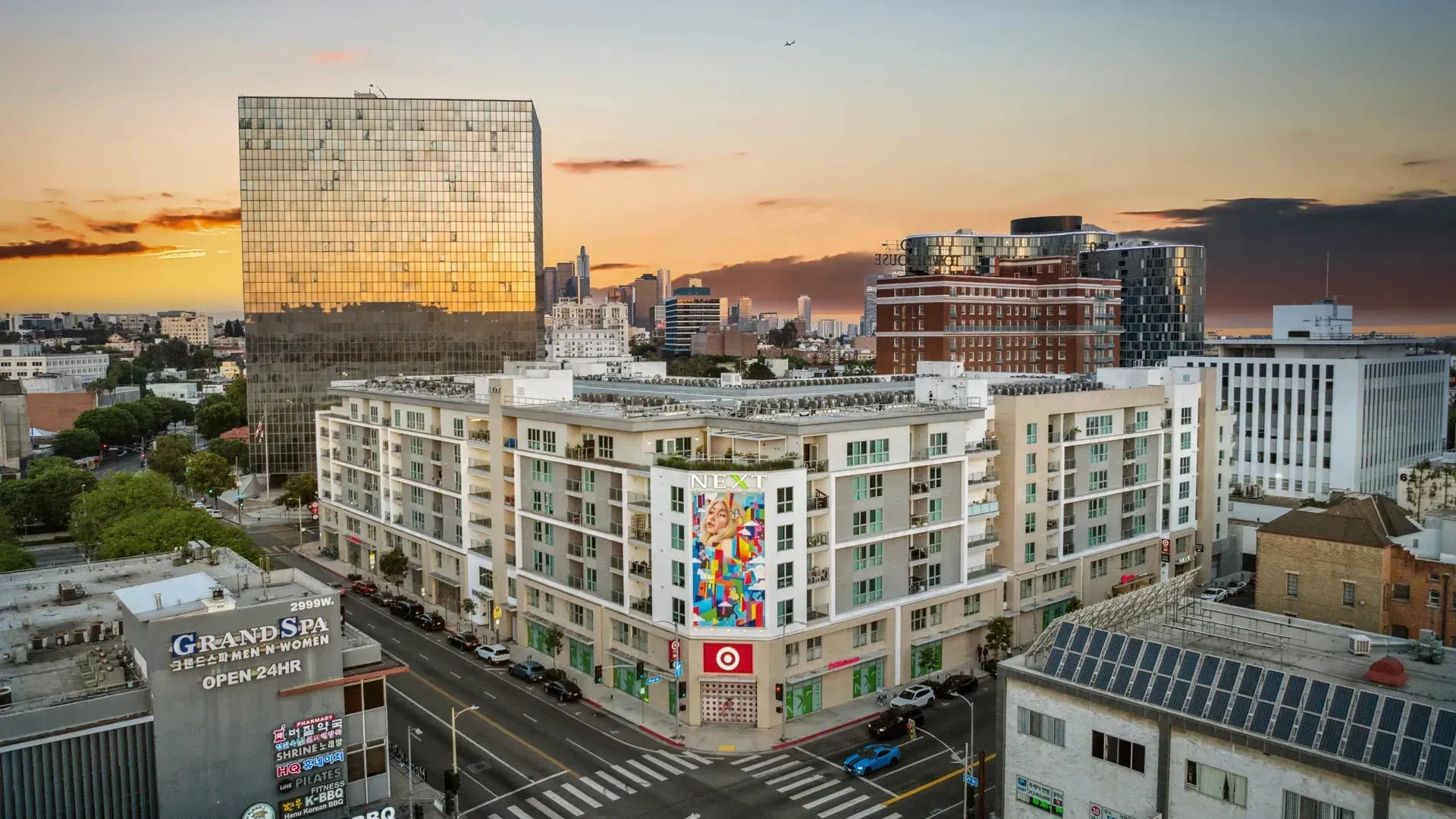 Aerial view of a modern apartment building with a colorful mural and Target store on the corner, during sunset.