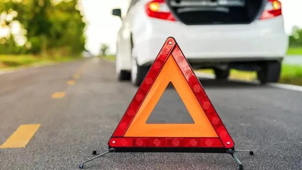 A car is sitting on the side of the road next to a warning triangle.