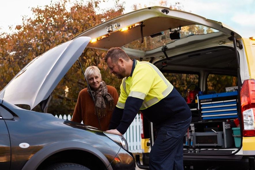 A man is working on the hood of a car while a woman looks on.
