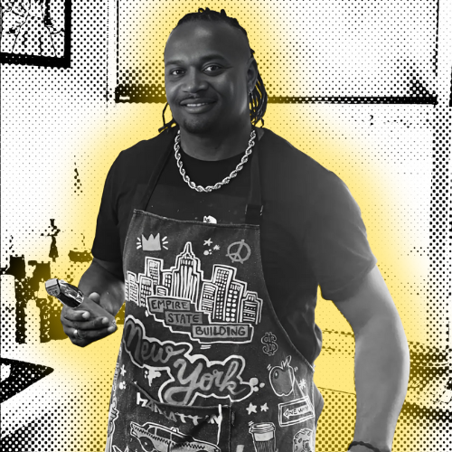 Professional portrait of Greg Williams, founder of The Fade Brothers in Indianapolis, wearing a custom New York themed barber apron and holding professional hair clippers.