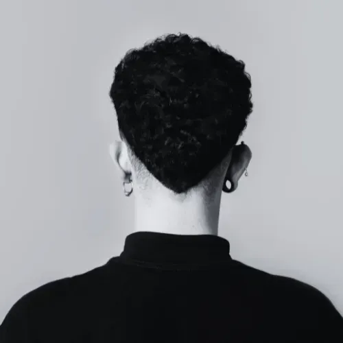 Person, back view, short, dark curly hair, black turtleneck, ear piercings.
