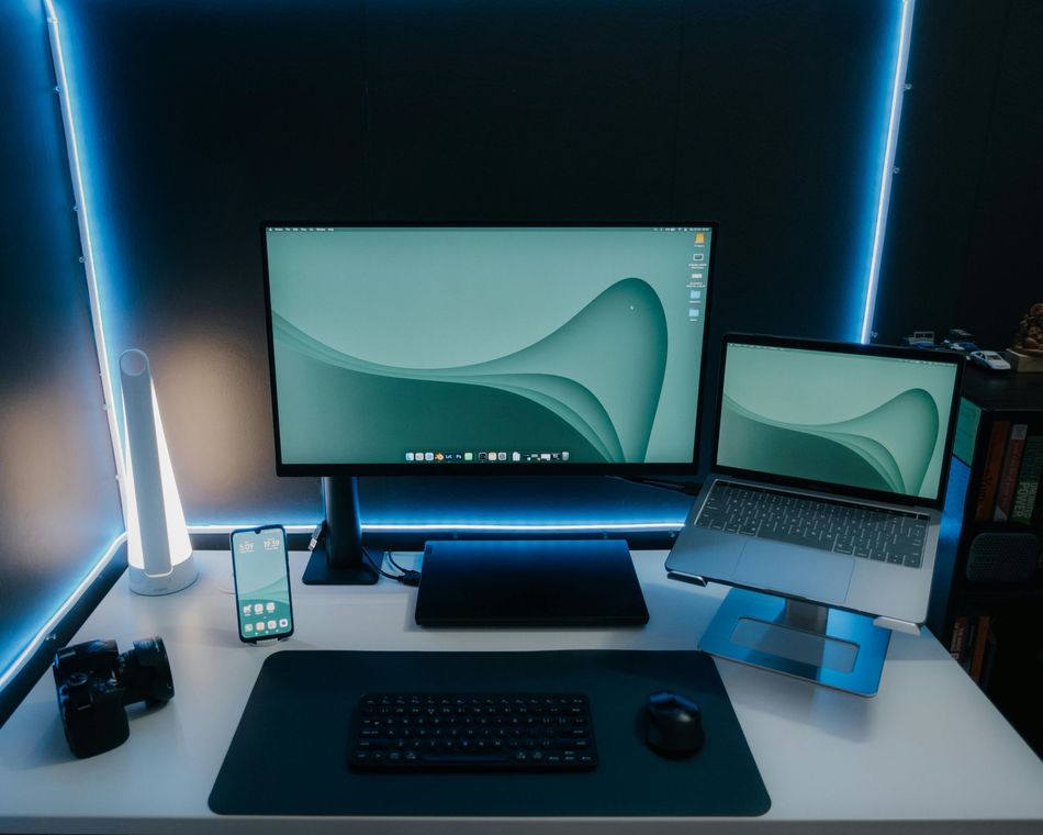 Modern desk setup with dual monitors, laptop, keyboard, mouse, phone, and blue LED lighting