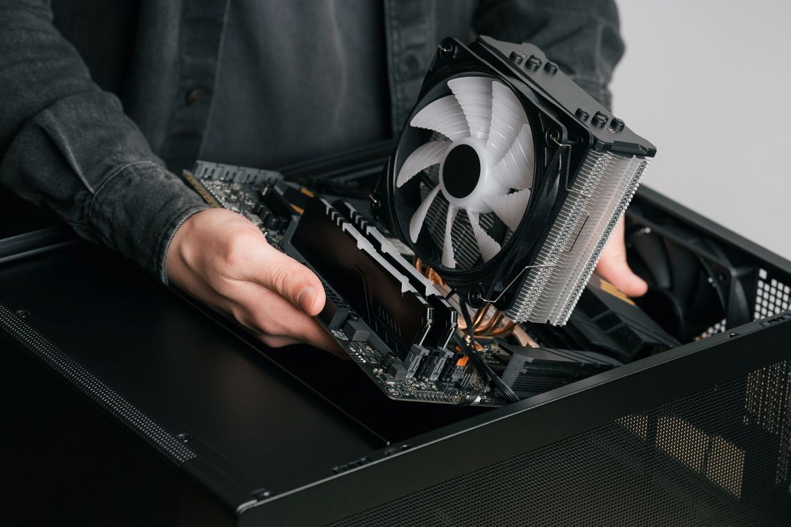 Person holding a graphics card with a large white cooling fan over an open computer case