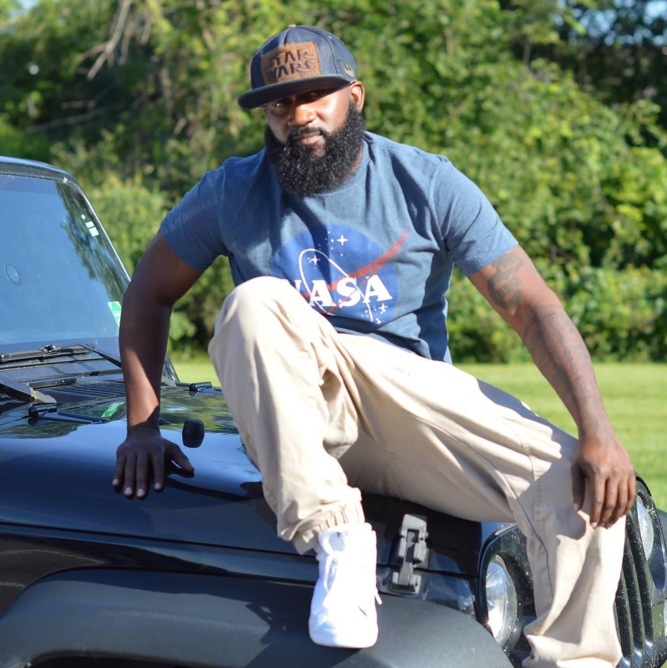 A man wearing a nasa shirt sits on the hood of a jeep