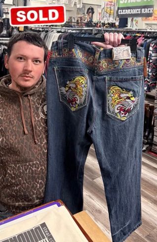 Man holding up a pair of blue jeans with colorful embroidered back pockets in a clothing shop