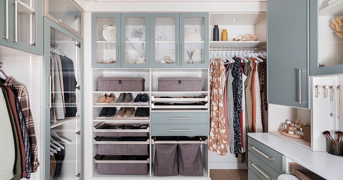 Walk-in closet with blue-grey cabinets, hanging clothes, drawers, and shoe storage, light wood flooring.