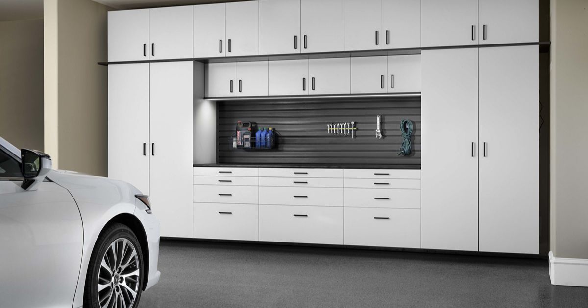 White garage storage cabinets and work surface with tools and a car.