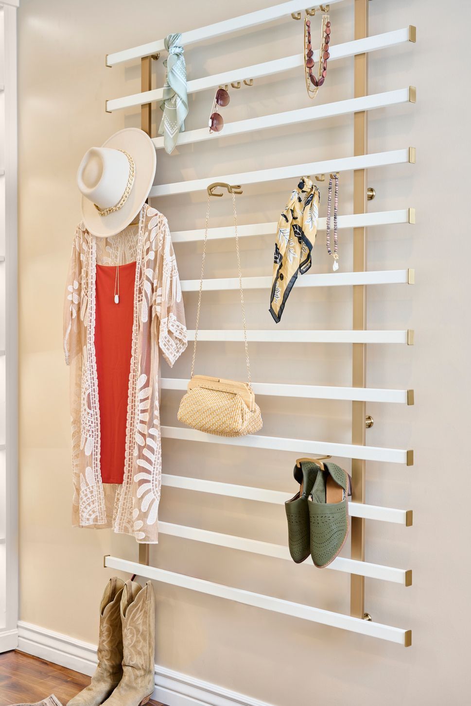 White wall-mounted slatted rack holding hats, scarves, a woven bag, and green boots in a tidy entryway