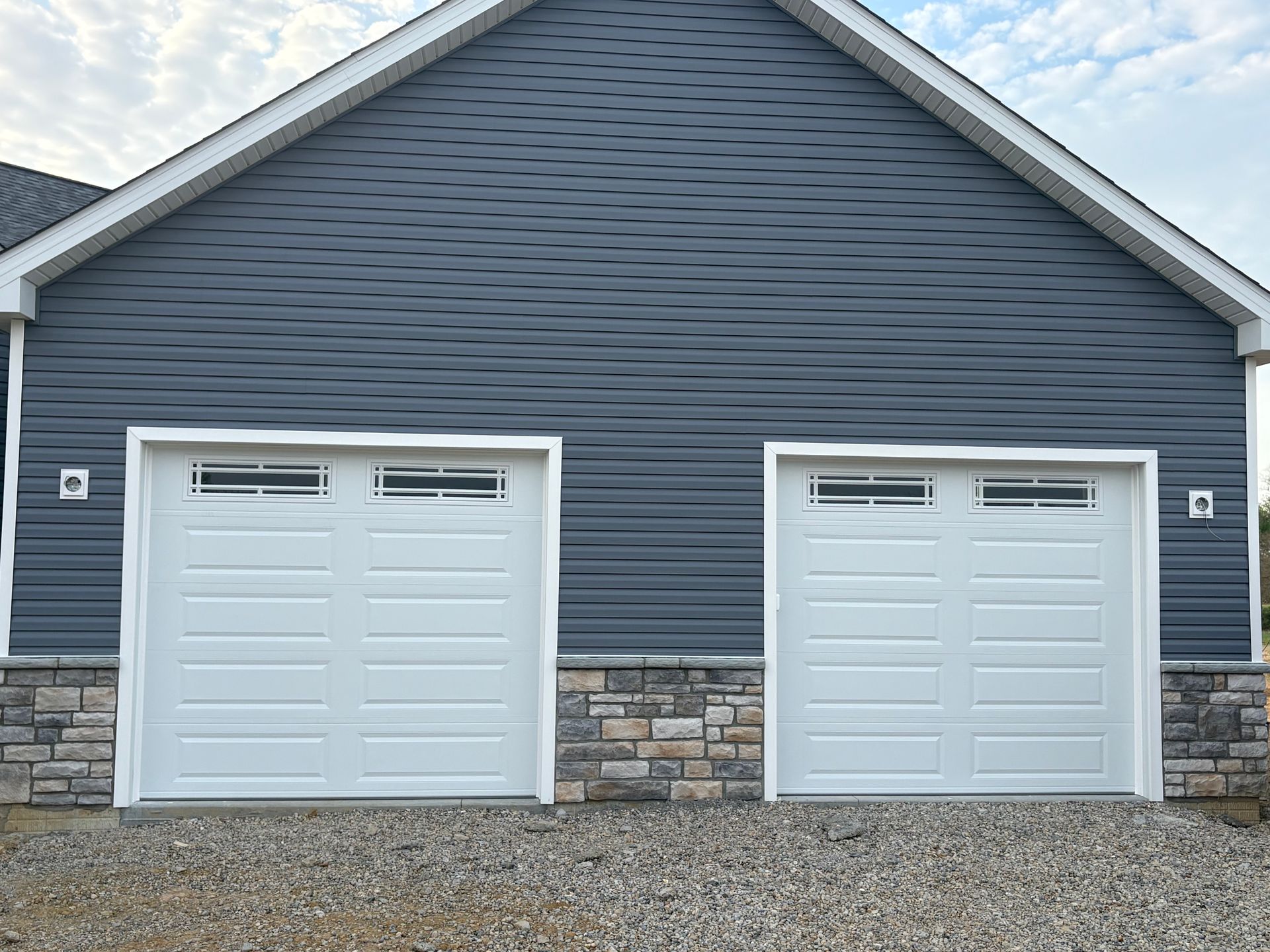 Blue house with two white garage doors and a stone base under a peaked roof. Blue house with two white garage doors and a stone base under a peaked roof.
