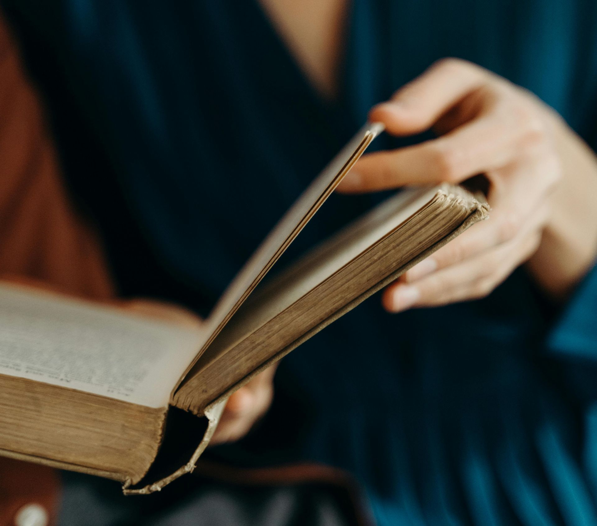 Hands holding an open book, with a page being turned in warm light