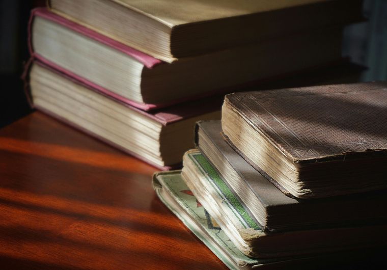 Stack of worn hardcover books on a wooden surface, lit by warm sunlight