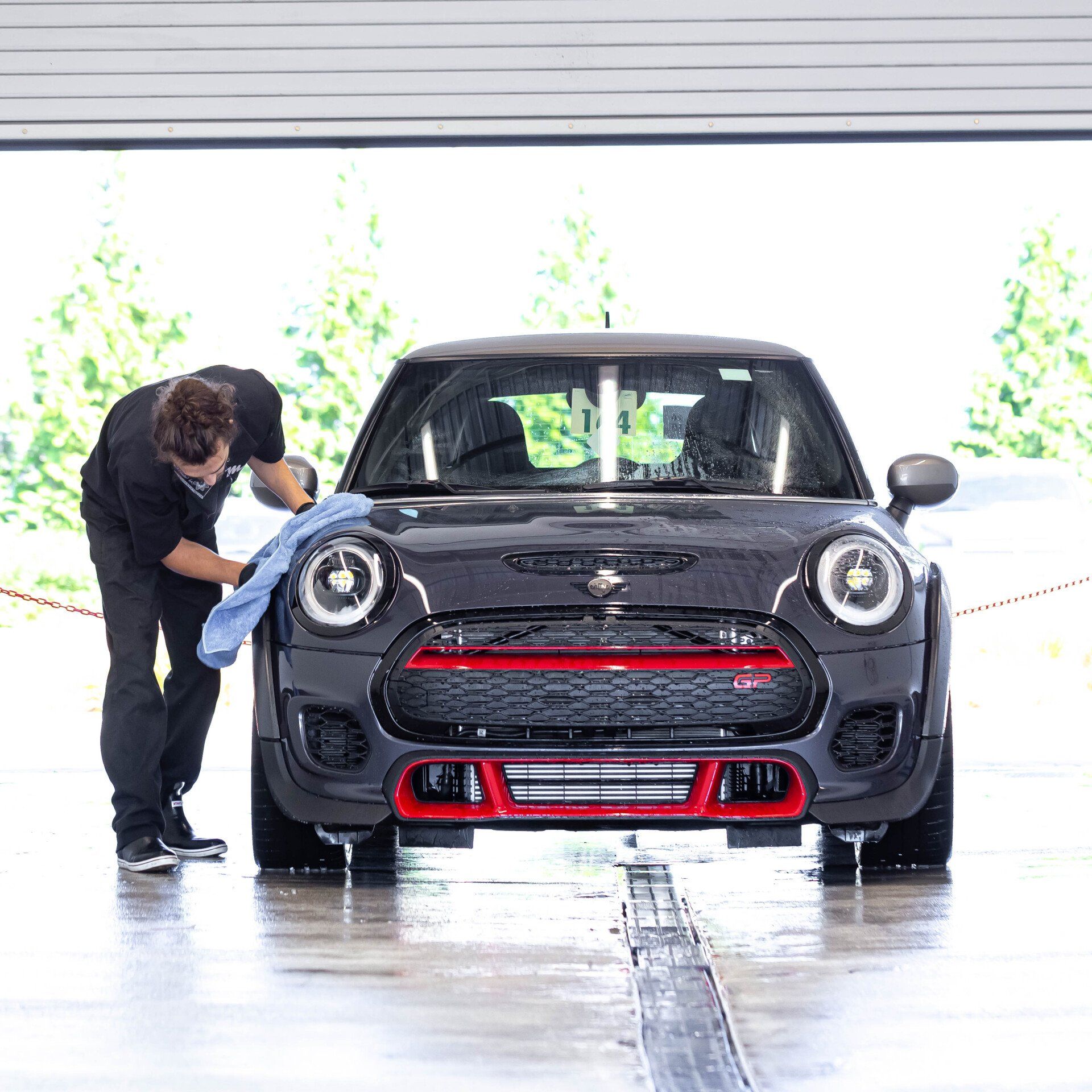 A man is cleaning a car with a towel in a garage.