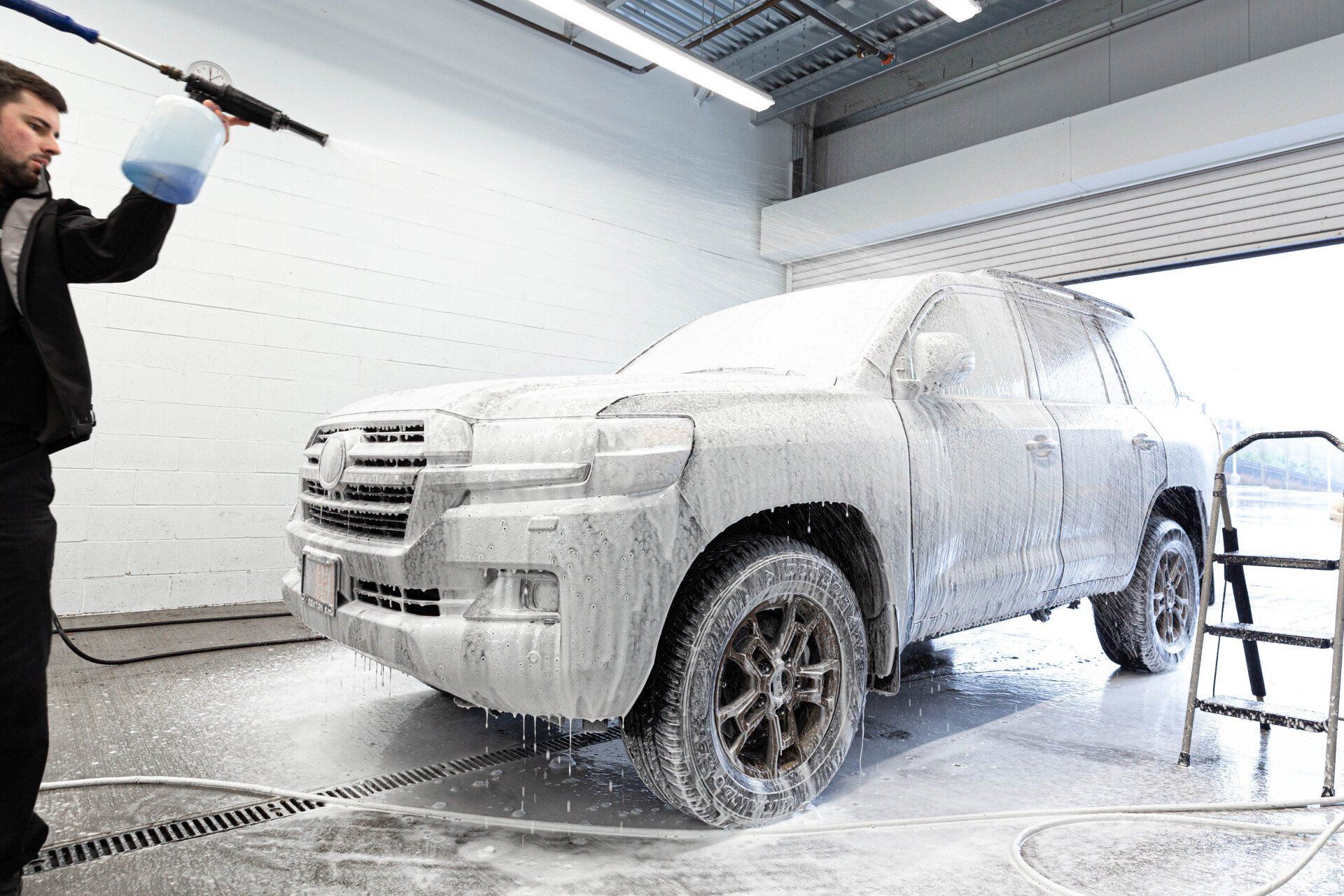 A man is washing a car with foam in a garage.