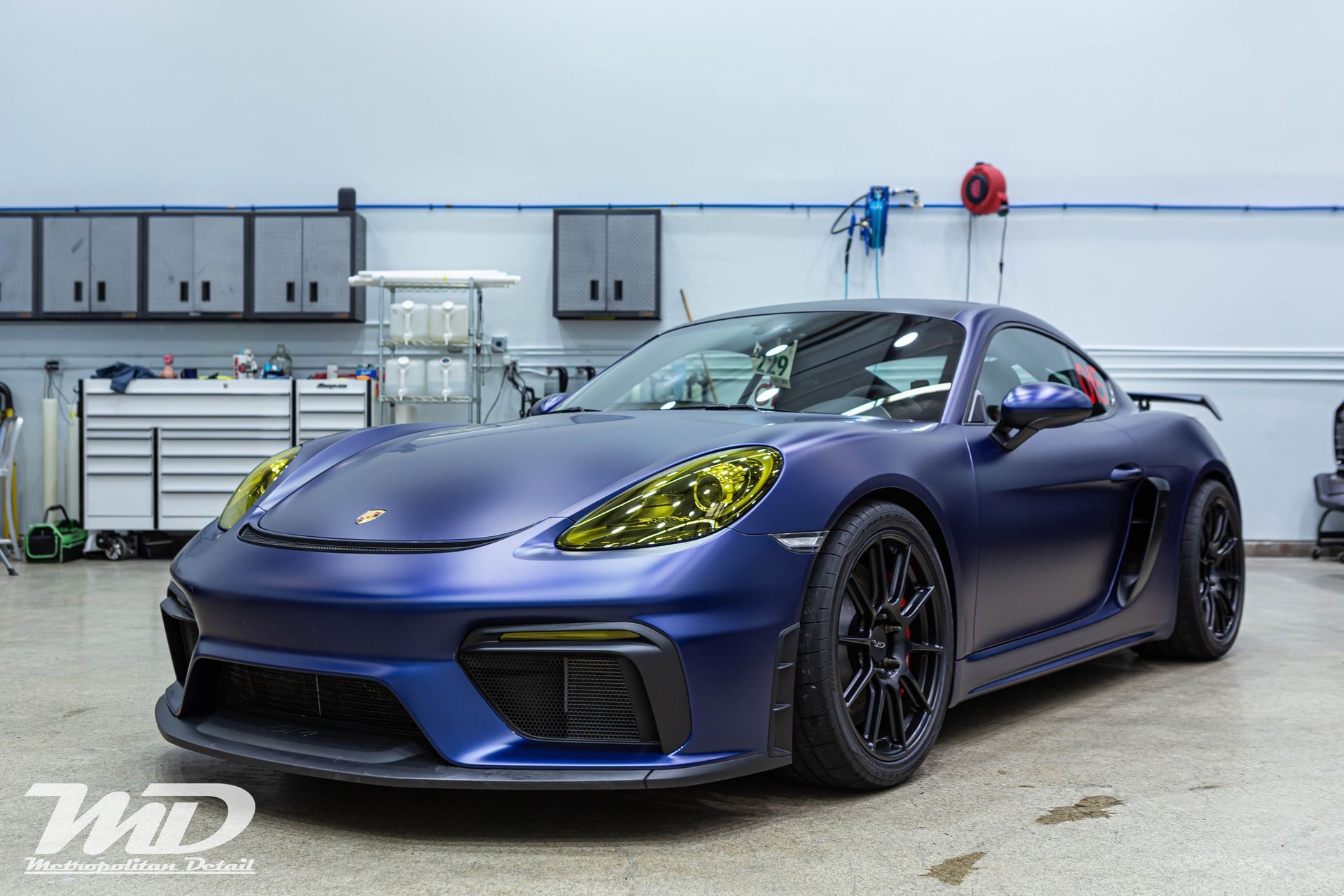 A blue porsche boxster gt4 is parked in a garage.