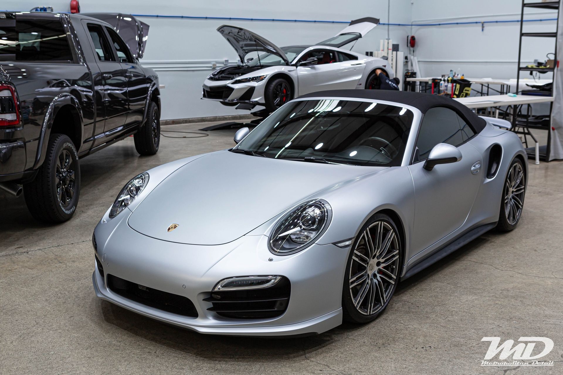 A silver porsche 911 turbo s convertible is parked in a garage.