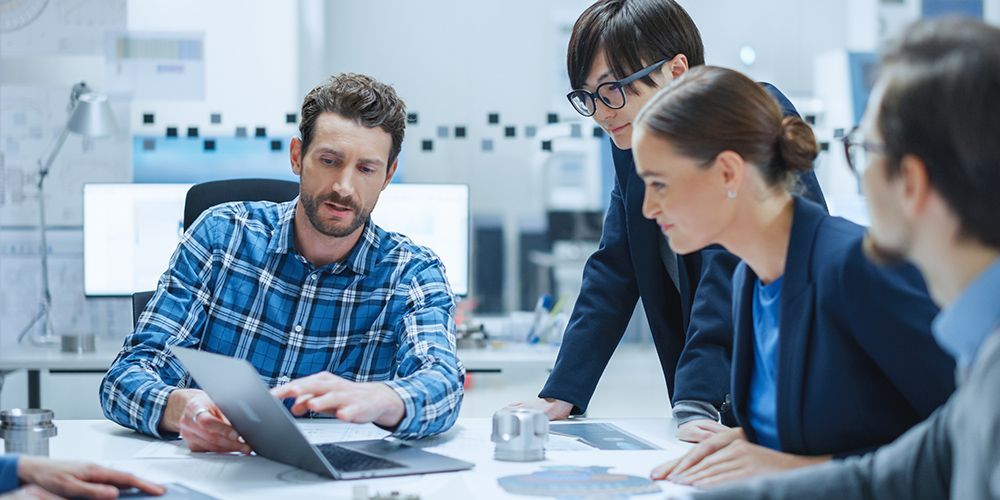 A group of people are sitting around a table looking at a laptop computer.