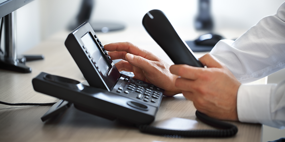 A man is typing on a telephone while sitting at a desk.