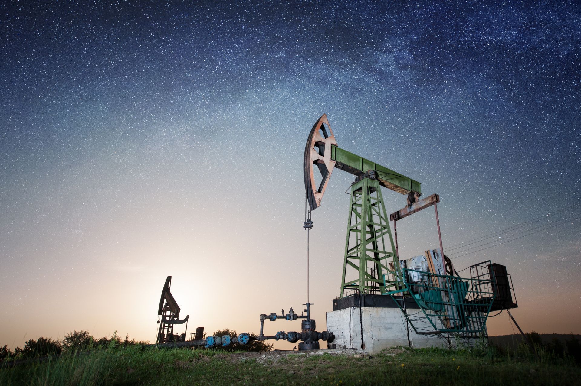 An oil pump is sitting in the middle of a field under a starry sky.