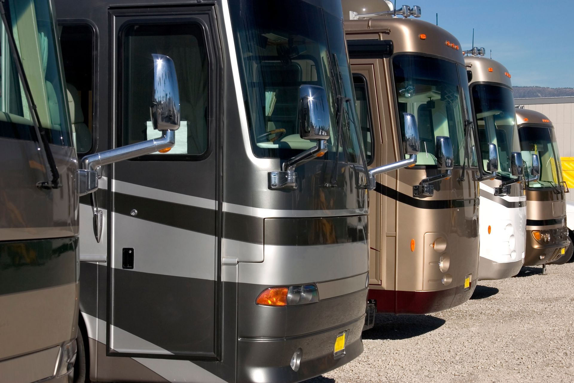 Row of parked motorhomes in silver, tan, and white at an outdoor lot